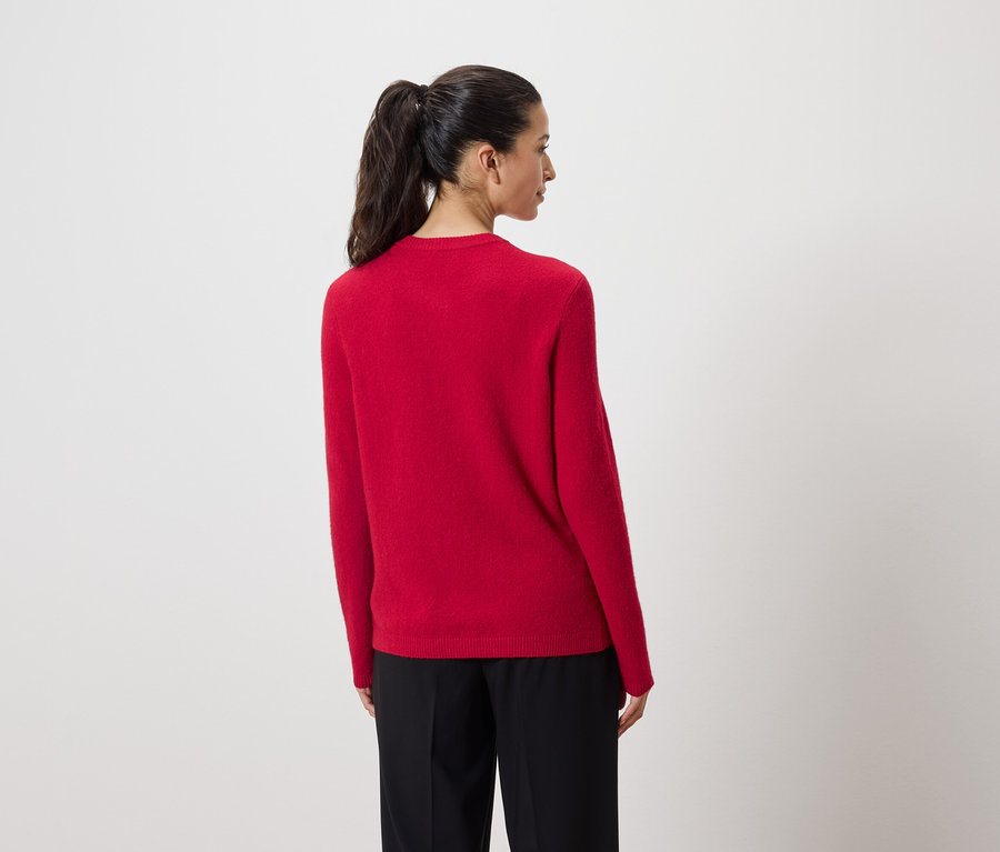 Une femme, dos à la caméra, porte un pull rouge et un pantalon noir.