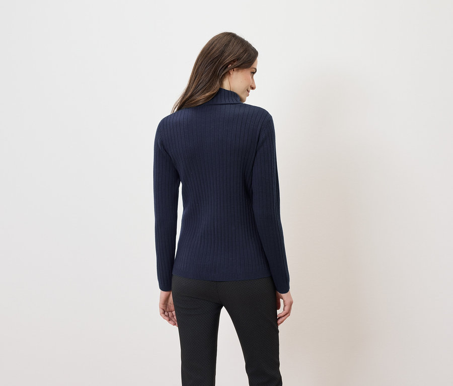 Vue arrière d'une femme aux longs cheveux bruns portant un pull à col roulé bleu marine et un pantalon noir.