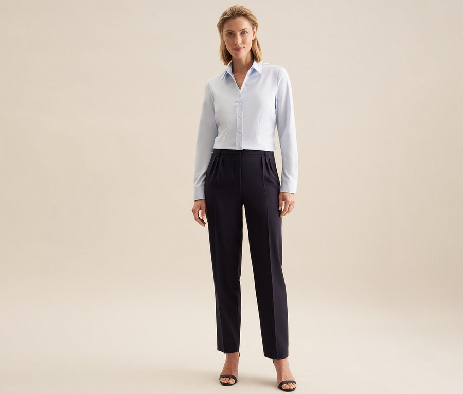 Femme debout, portant un chemisier en tulle Seidensticker bleu clair, un pantalon foncé et des sandales foncées.
