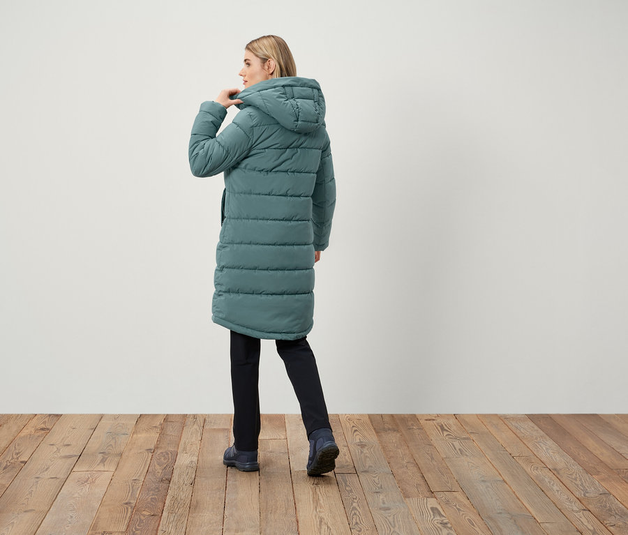 Femme portant un long manteau matelassé à capuche, dos à la caméra.