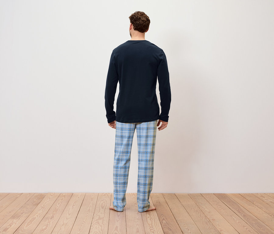 Un homme vu de dos porte un pyjama bleu à manches longues et un pantalon à carreaux bleus.