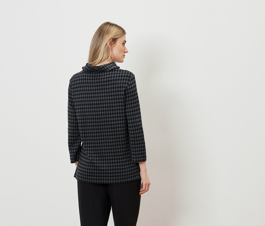 Une femme vue de dos porte un chemisier pied-de-poule et un pantalon noir.