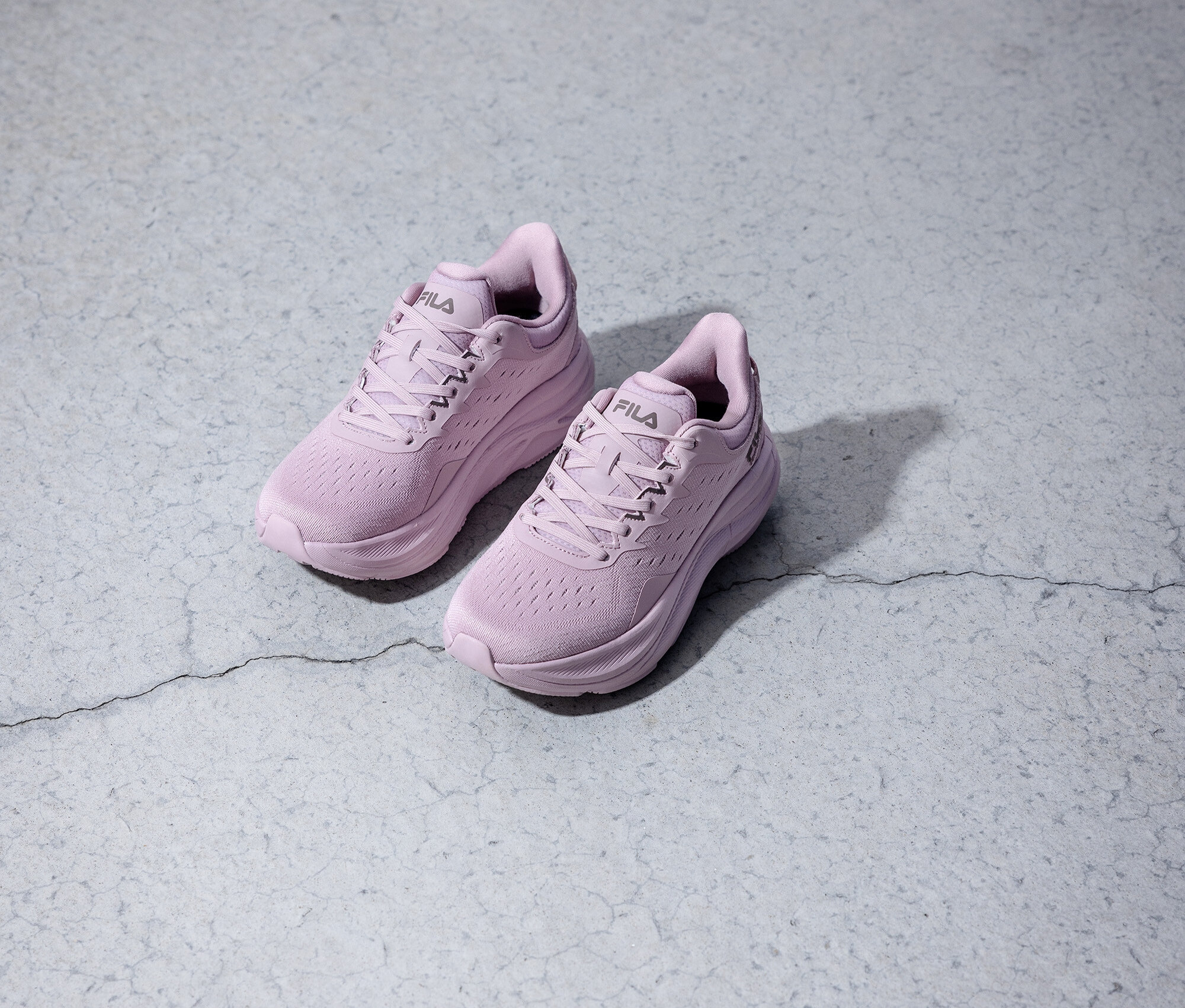 Deux chaussures de course Fila violettes posées sur un fond gris.