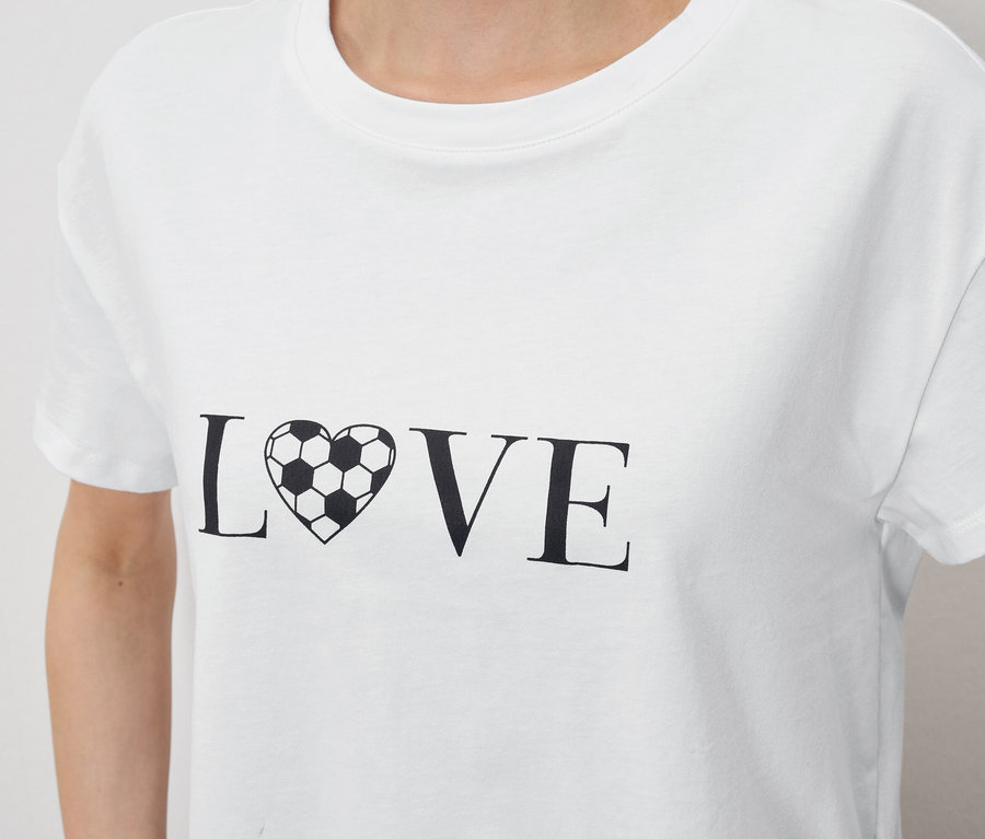 Gros plan sur une personne portant un t-shirt blanc avec l'inscription « LOVE », le « O » étant remplacé par un cœur en forme de ballon de football.