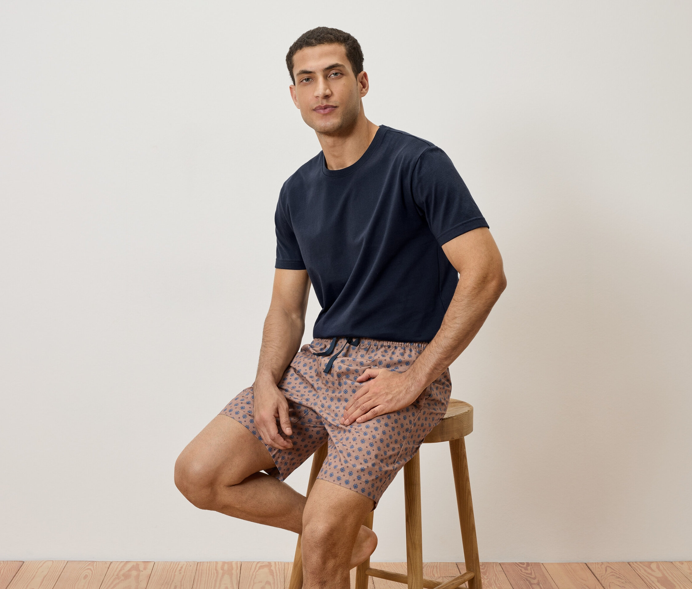 Homme assis sur un tabouret, portant un t-shirt bleu marine et un short à motifs.