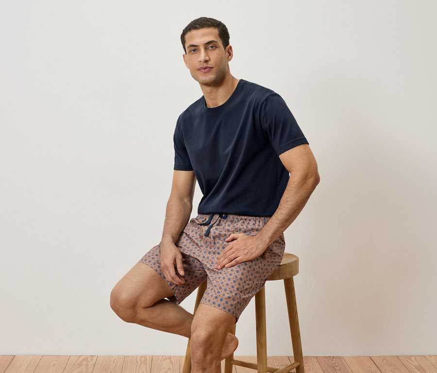 Homme assis sur un tabouret, portant un t-shirt bleu marine et un short à motifs.