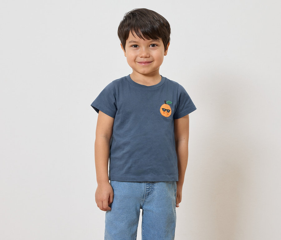 Un enfant porte un t-shirt bleu avec un imprimé orange et un jean.