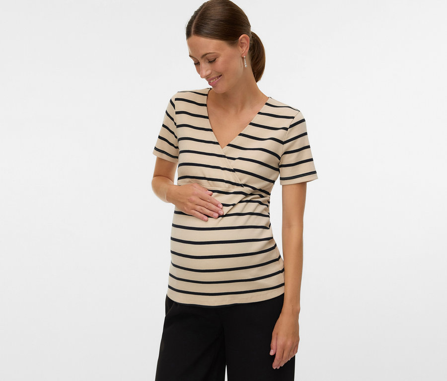 Une femme avec une queue de cheval porte un t-shirt de grossesse rayé MAMALICIOUS «
MLLANE TESS » et un pantalon noir, tout en touchant son ventre.