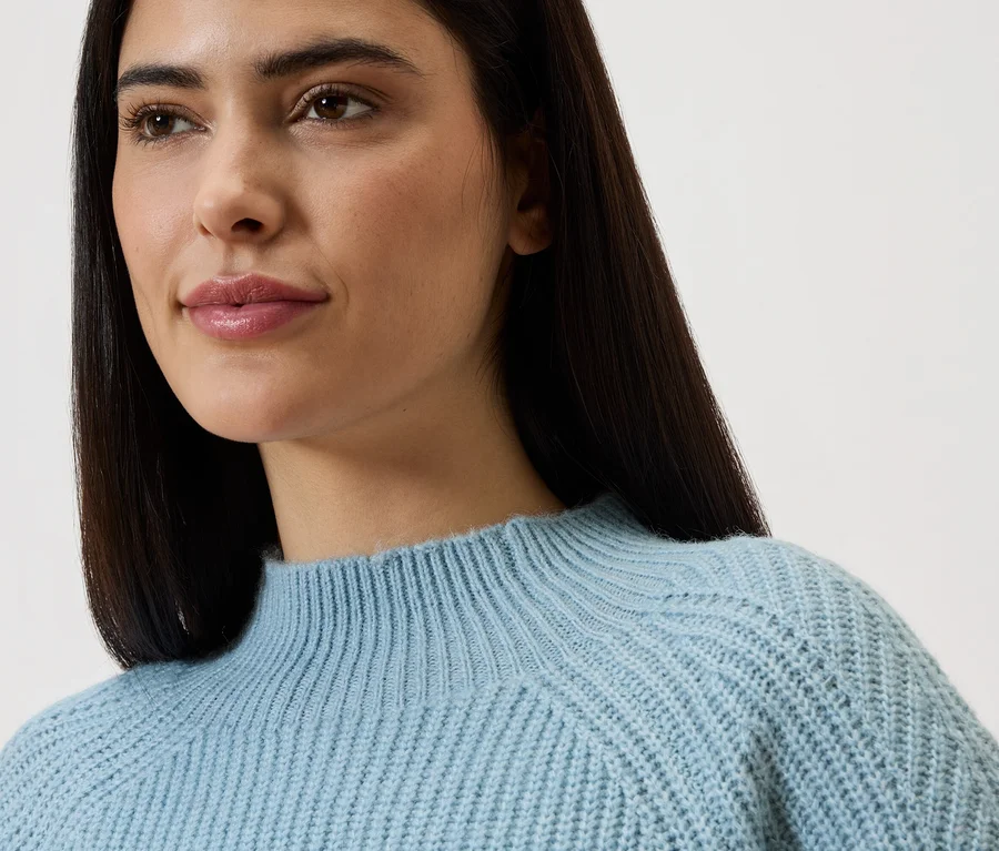 Portrait rapproché d'une femme aux longs cheveux foncés portant un pull en tricot bleu clair.