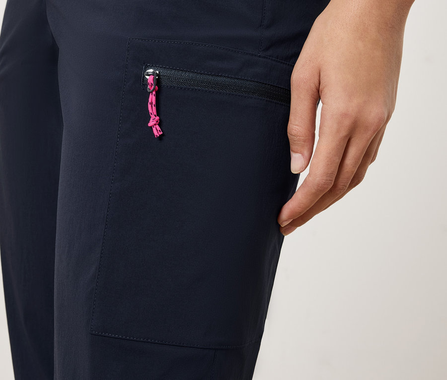 Gros plan d'une personne portant un pantalon bleu marine avec une poche zippée et un cordon de serrage rose.
