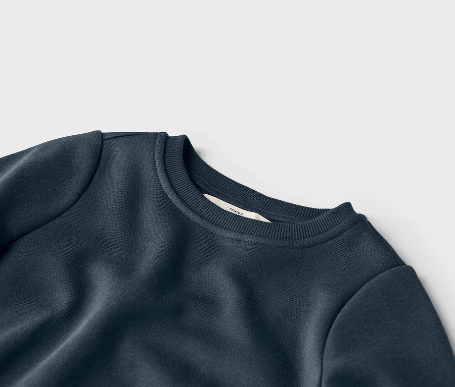 Vue détaillée d'un sweat-shirt bleu marine à col rond avec une étiquette de la marque Tchibo au niveau du col.