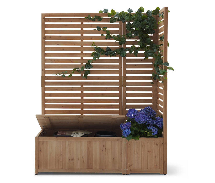 Structure en bois avec des lattes horizontales, partiellement recouverte de lierre. Un coffre en bois avec un couvercle ouvert se trouve en dessous.