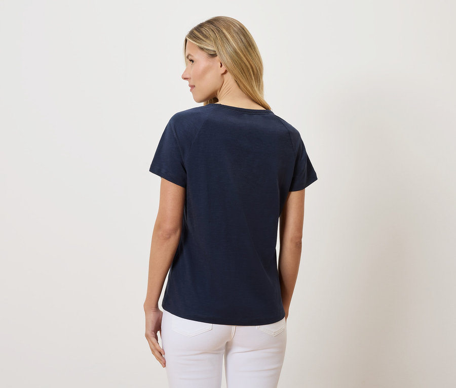 Vue arrière d'une femme aux cheveux blonds portant un t-shirt bleu marine et un jean blanc.