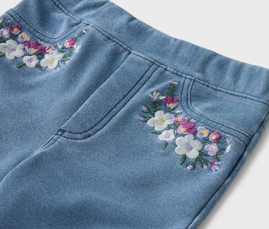 Gros plan d'un jean bleu clair avec des broderies florales sur la ceinture et la poche.