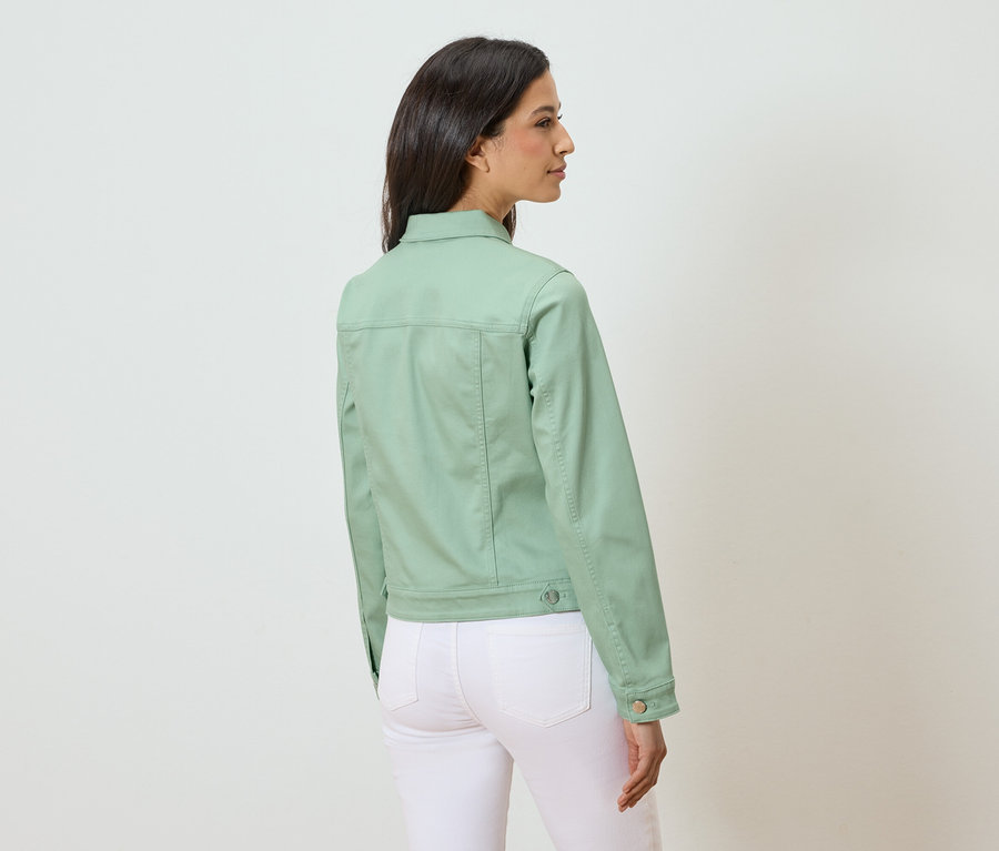 Femme portant une veste en jean vert clair et un pantalon blanc, vue de dos.