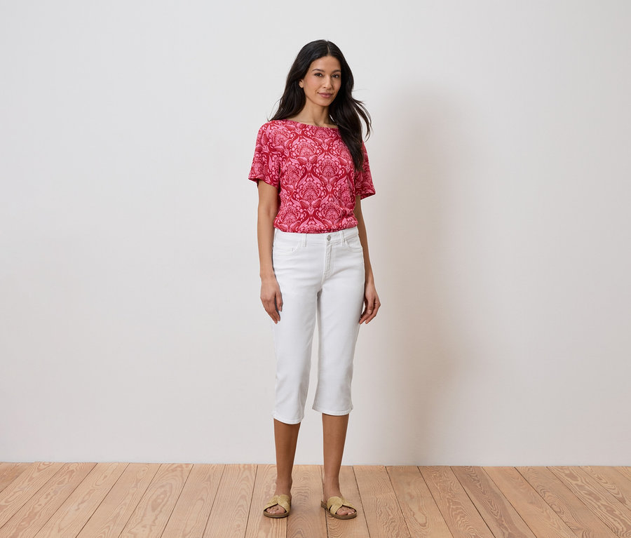 Une femme se tient devant un mur portant un haut rouge et un pantalon blanc.