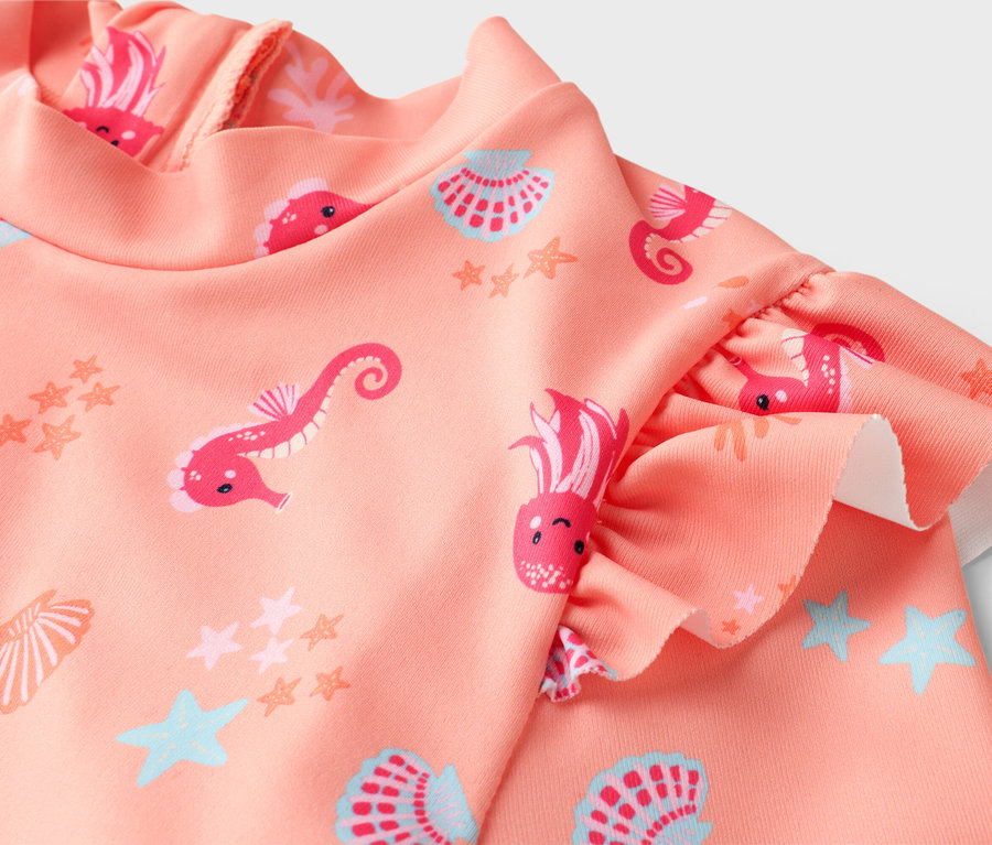 Gros plan d'un maillot de bain rose pour enfant avec des manches à volants et un motif intégral d'hippocampes, de méduses, d'étoiles et de coquillages.