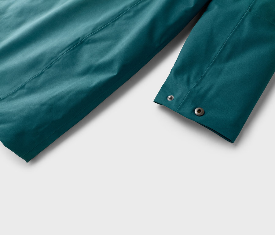 Gros plan sur la manche turquoise d'une veste avec deux boutons-pression argentés sur un fond blanc.