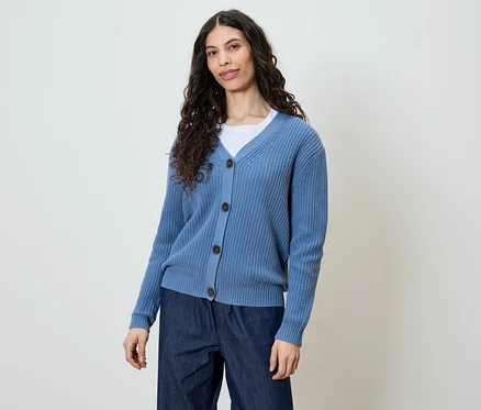 Femme aux longs cheveux bouclés et foncés portant un cardigan bleu et un jean foncé.