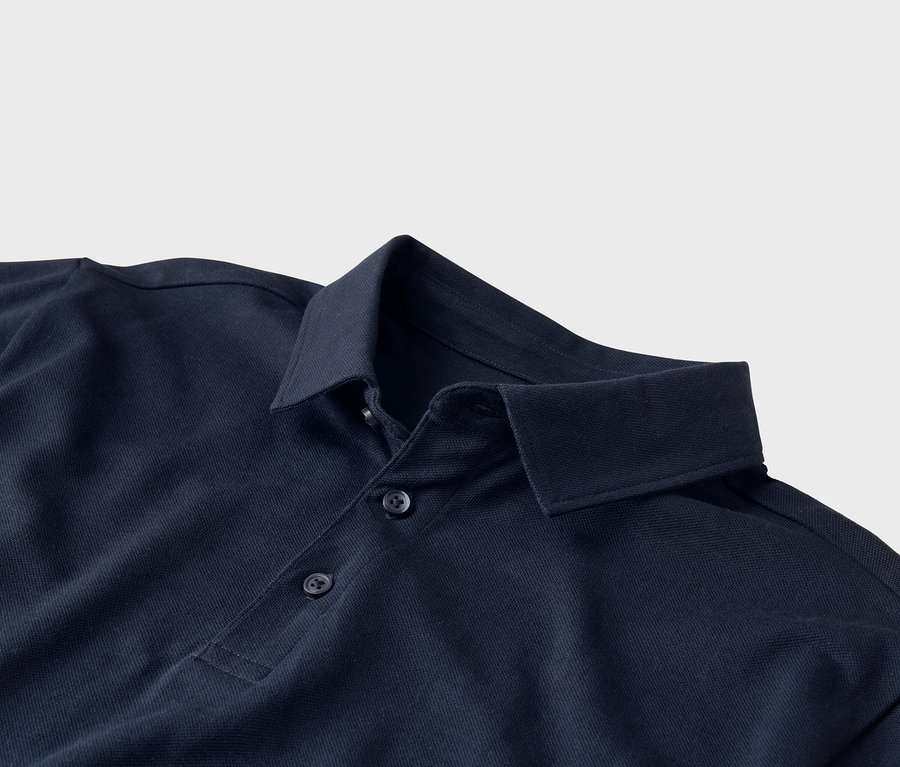 Gros plan d'un polo bleu marine avec un col et trois boutons sur un fond gris clair.