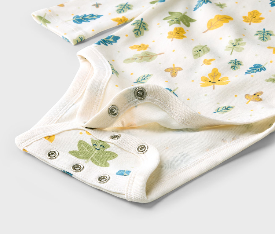 Gros plan sur un body blanc pour bébé avec des feuilles colorées et des boutons-pression à l'entrejambe.