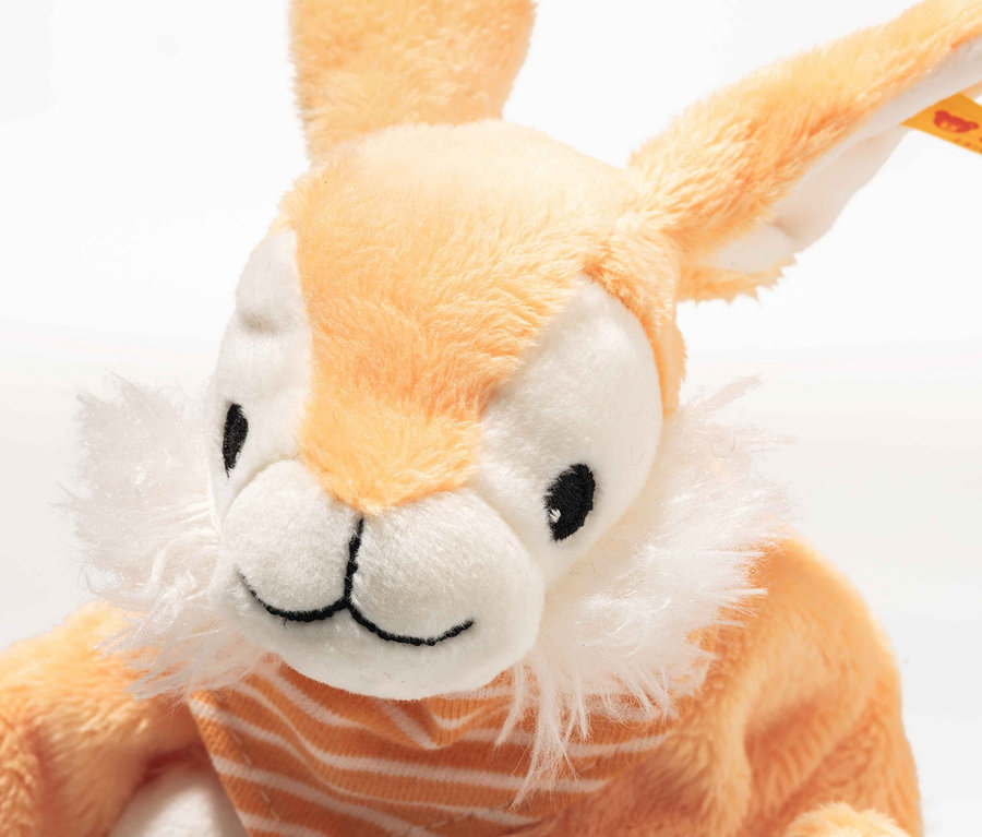 Gros plan d'un lapin en peluche orange portant un foulard rayé.