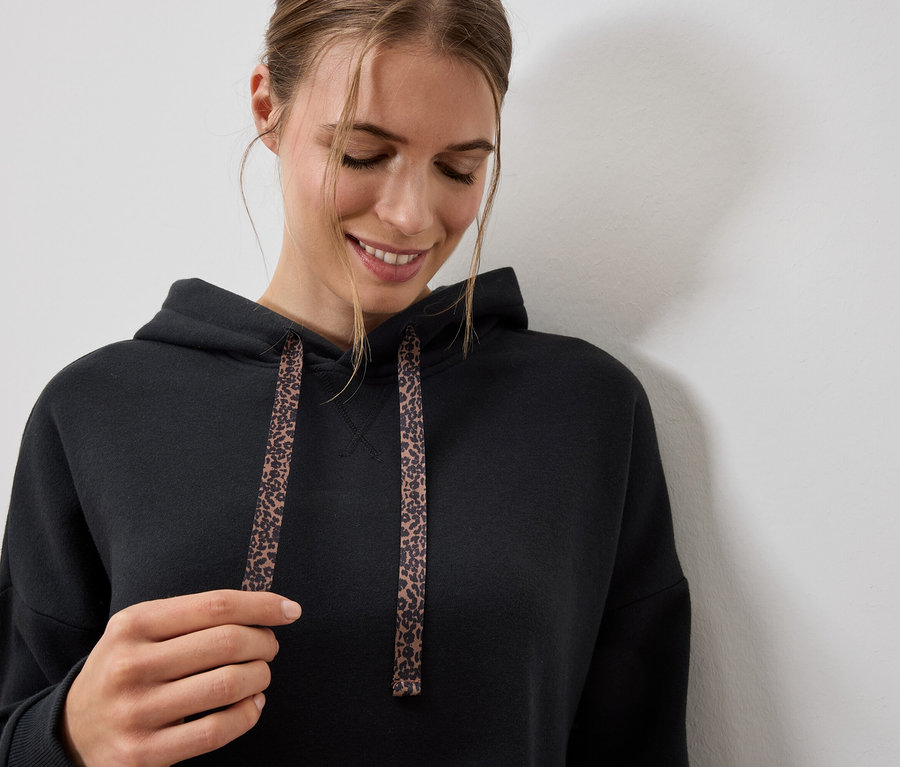 Femme portant un sweat à capuche noir avec des cordons à motif léopard.