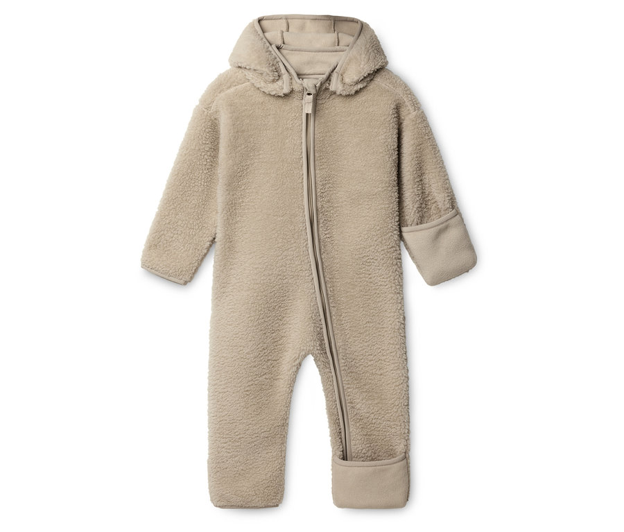 Une combinaison de bébé en teddy beige avec capuche et fermeture éclair est posée sur un fond blanc.