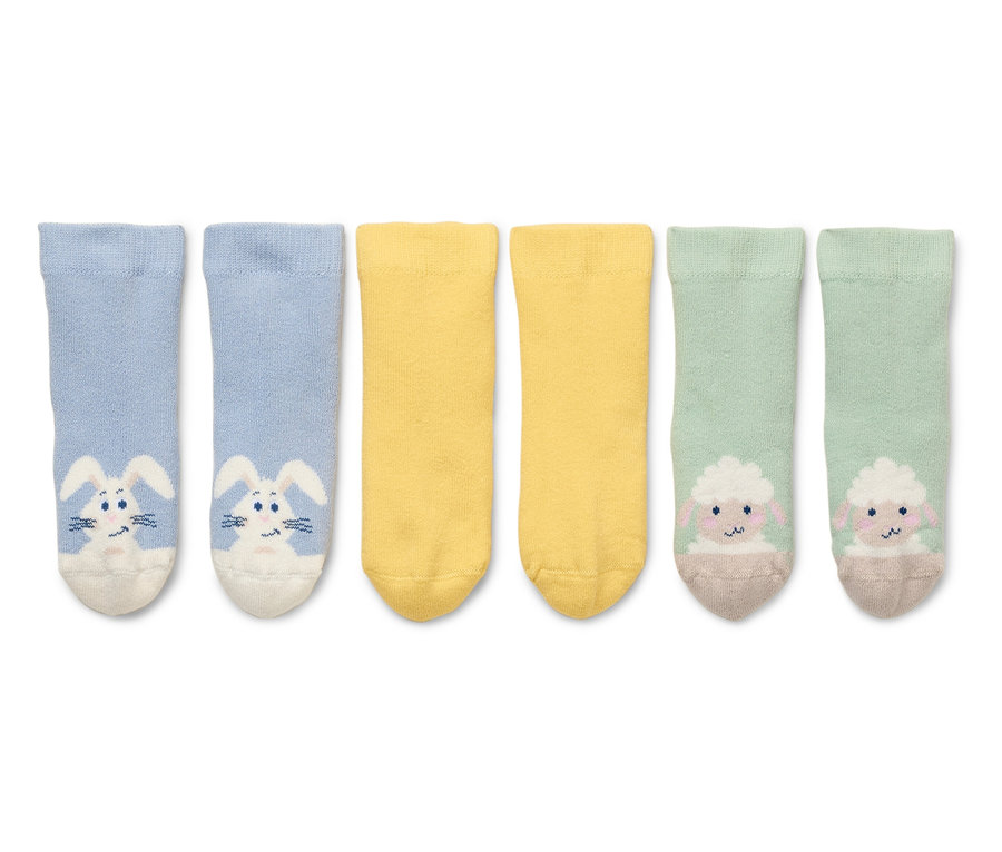 Deux chaussettes bleues avec des lapins, deux chaussettes jaunes et deux chaussettes vertes avec des moutons sont posées sur un fond blanc.