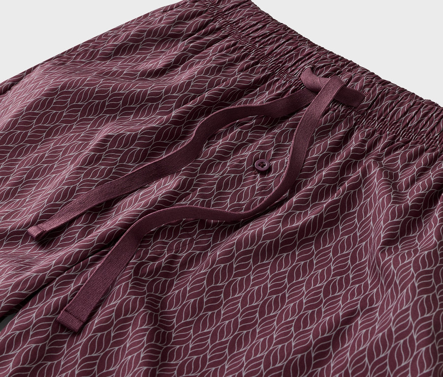 Gros plan d'un pantalon de pyjama bordeaux avec un motif de feuilles blanches, une taille élastique et un cordon de serrage bordeaux.