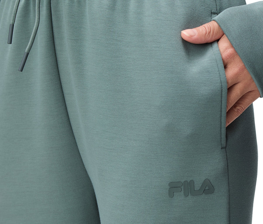Gros plan sur une personne portant un pantalon de jogging Fila vert avec une taille élastique et un cordon de serrage, ainsi qu'une main dans sa poche.