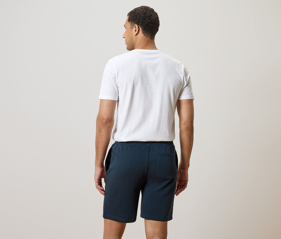 Vue arrière d'un homme portant un t-shirt blanc et un short bleu.