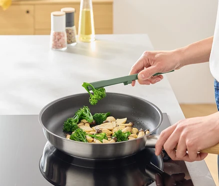 Une personne fait frire du brocoli et des champignons dans une poêle à l'aide d'un ustensile de cuisine vert.