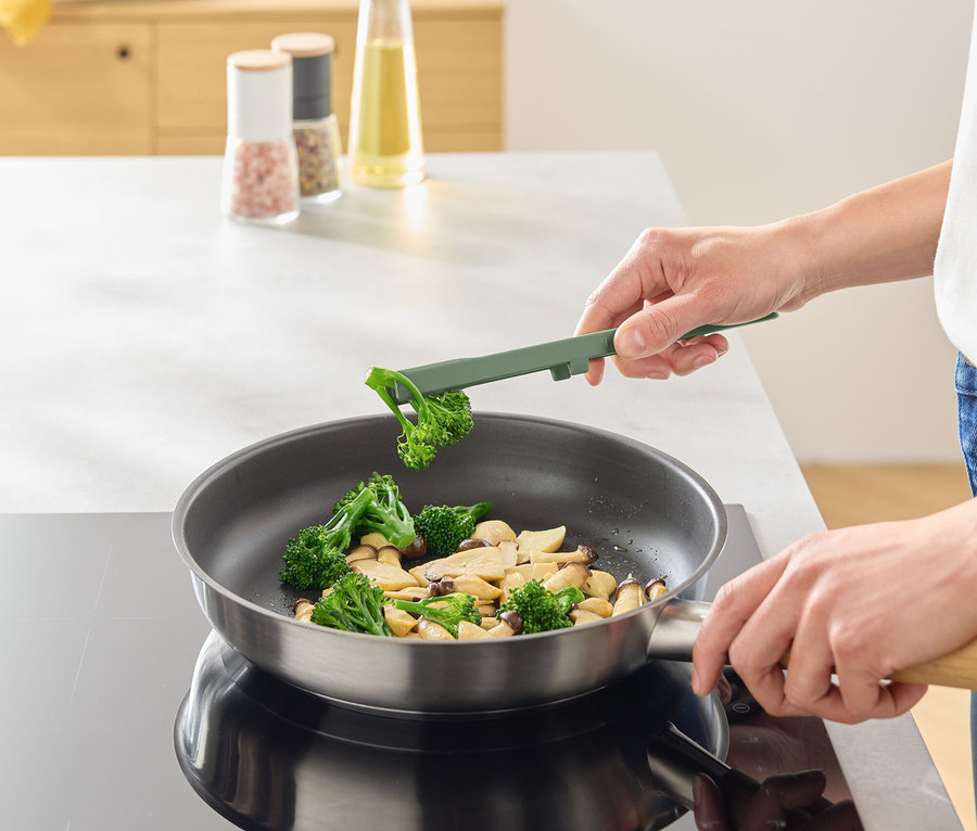 Une personne fait frire du brocoli et des champignons dans une poêle à l'aide d'un ustensile de cuisine vert.