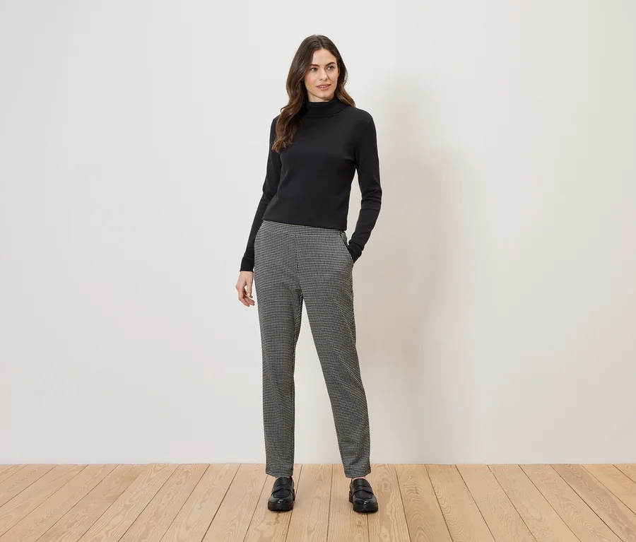 Femme portant un pull à col roulé noir et un pantalon à carreaux noir et blanc, avec des mocassins noirs.