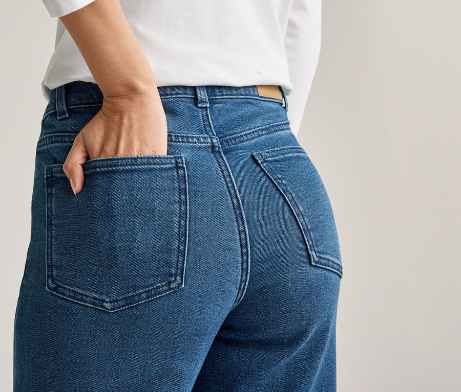 Femme, main dans la poche arrière d'un jean bleu, portant un haut blanc.