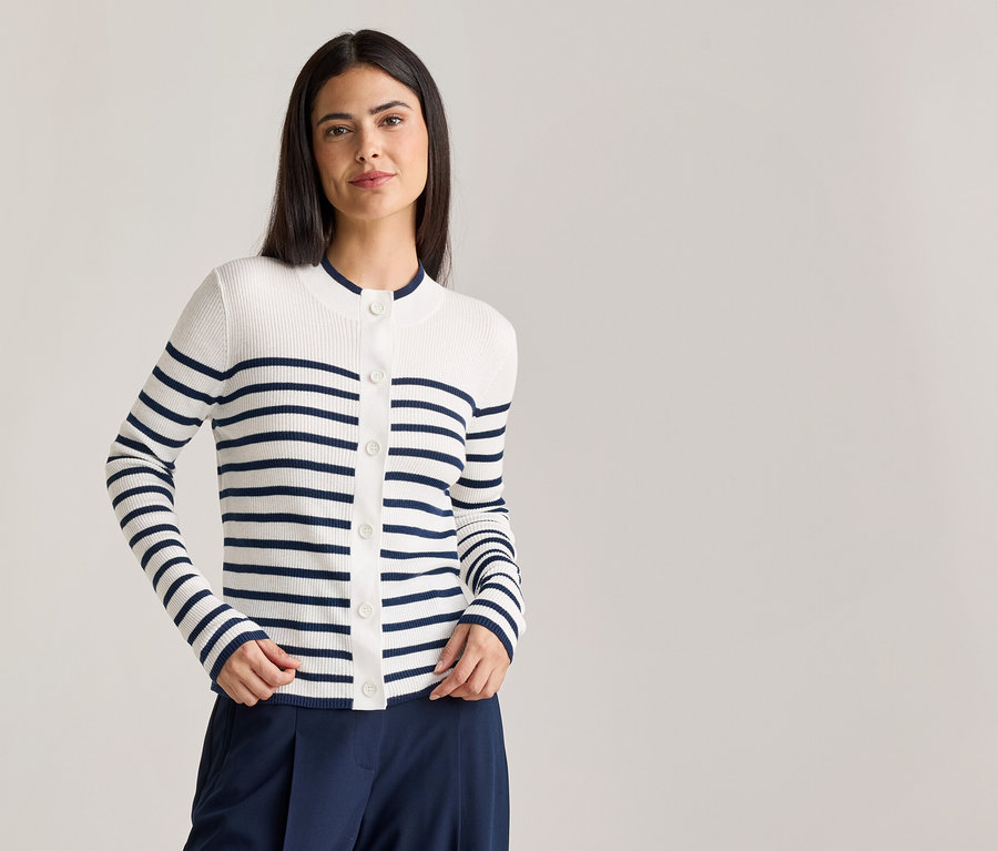 Une femme aux cheveux brun foncé porte un cardigan rayé blanc et bleu marine boutonné et un pantalon bleu marine.
