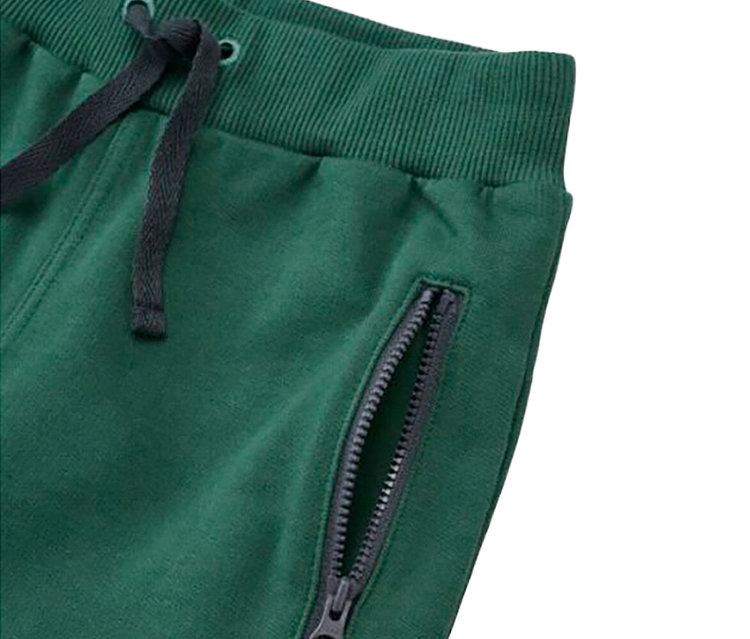 Gros plan d'un pantalon de jogging vert foncé avec une taille côtelée, un cordon de serrage gris foncé et une poche latérale zippée partiellement ouverte.