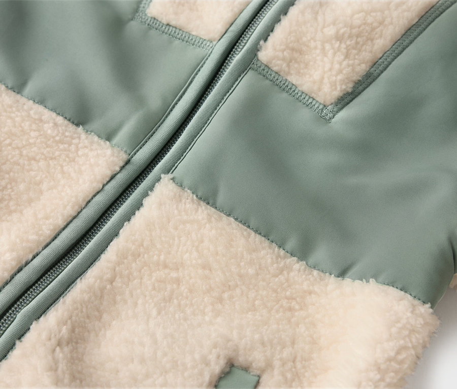 Gros plan d'une veste avec des empiècements en polaire vert clair et crème et une fermeture éclair au centre.