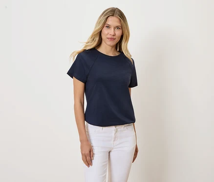 Une femme blonde porte un t-shirt bleu marine et un jean blanc.