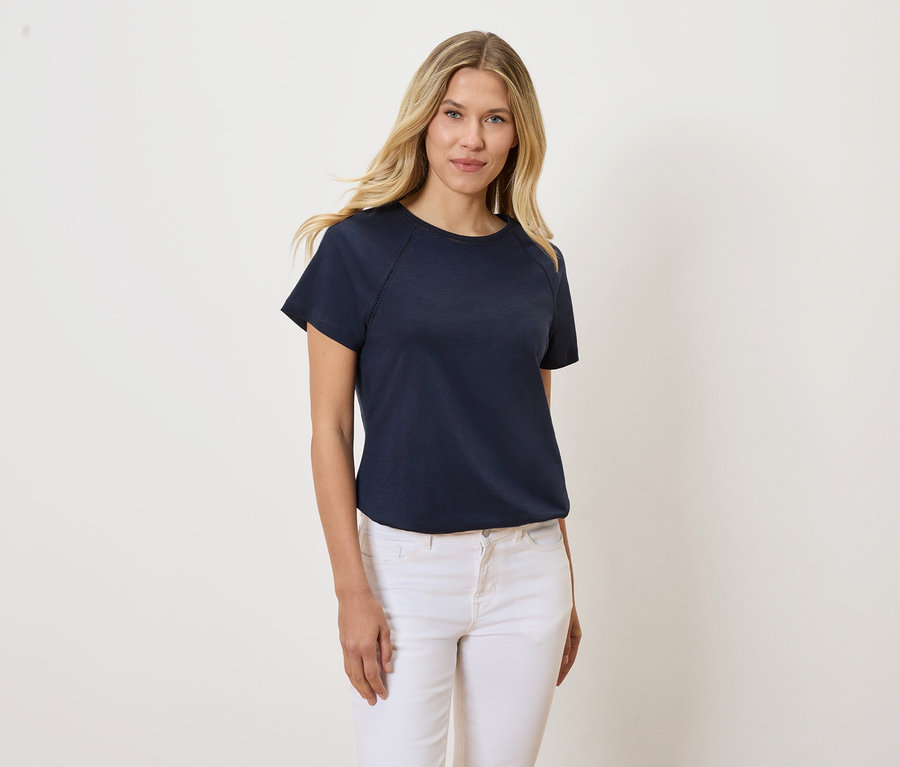 Une femme blonde porte un t-shirt bleu marine et un jean blanc.