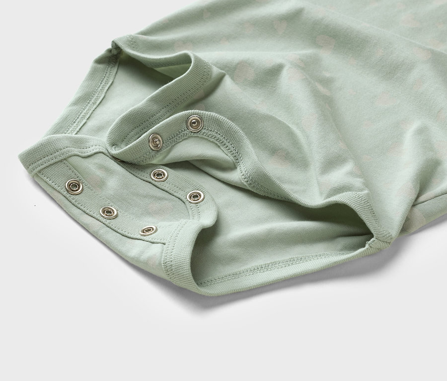 Gros plan sur un body bébé vert clair avec des boutons-pression.