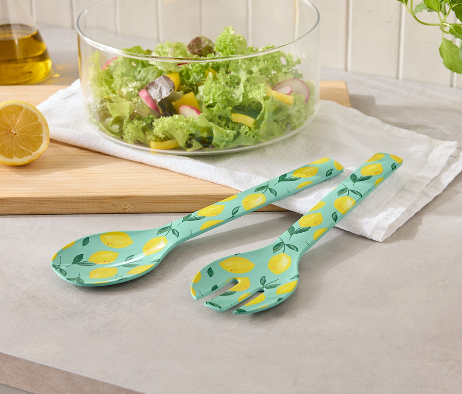 Ensemble de service à salade avec motif citron à côté d'un saladier et de citrons sur une table.