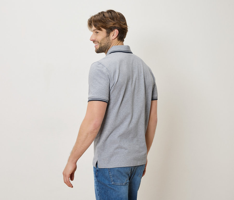 Homme de dos portant un polo gris et un jean, souriant.