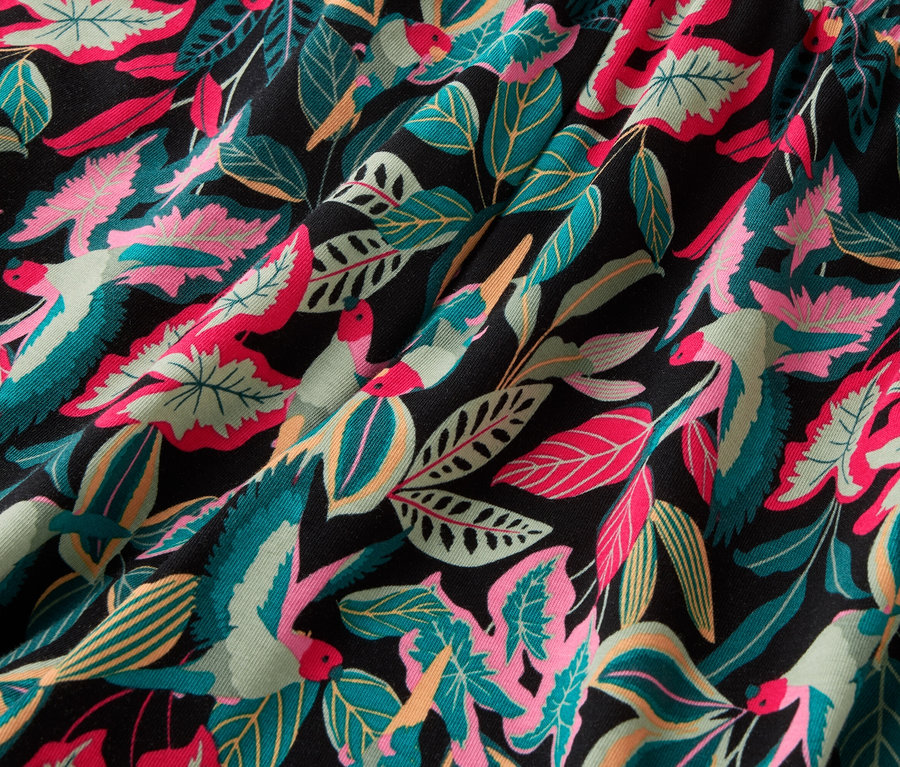 Gros plan d'un tissu avec un motif de feuilles et d'oiseaux colorés sur fond noir.