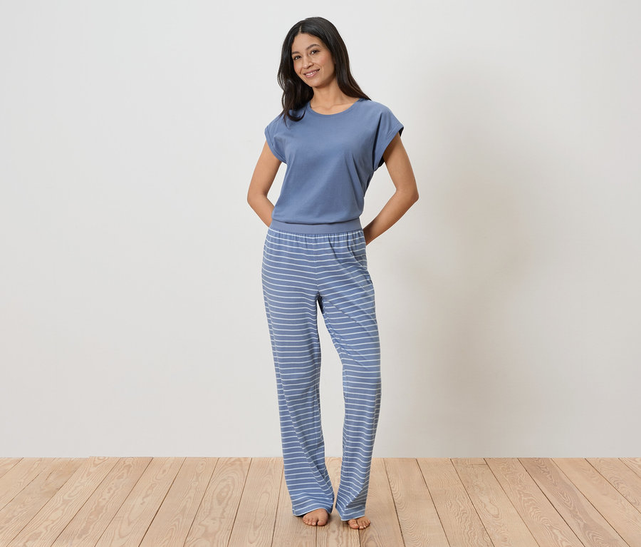 Femme portant un t-shirt bleu et un pantalon rayé posant devant un mur blanc.