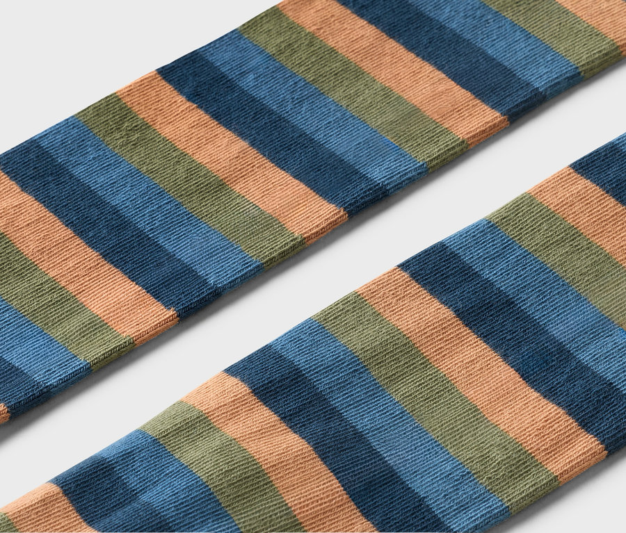 Gros plan de deux chaussettes rayées orange, bleu et vert sur fond gris.