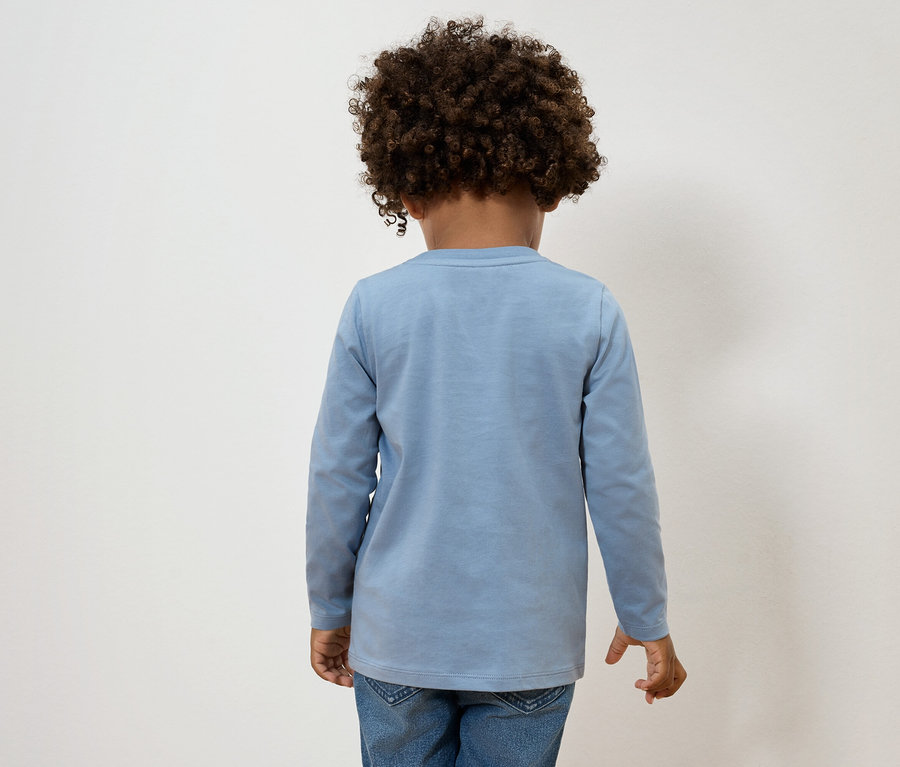 Vue arrière d'un enfant aux cheveux bouclés portant un haut à manches longues bleu clair et un jean.