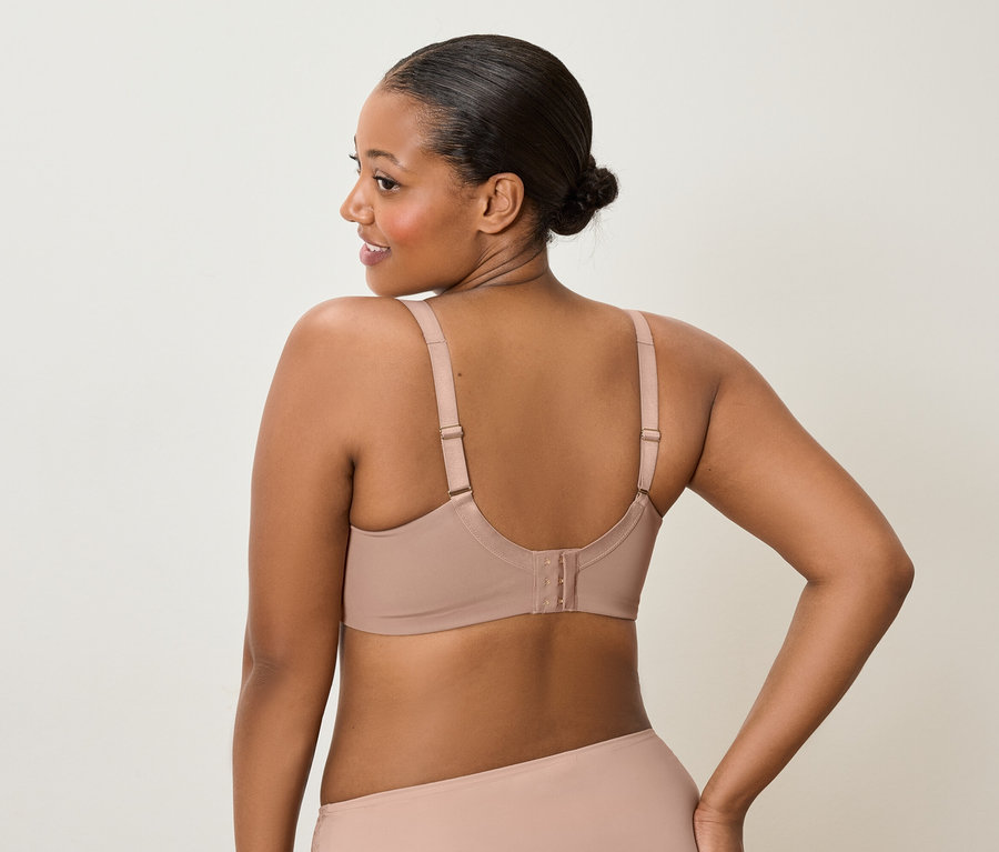 Vue de dos d'une femme à la peau foncée portant un chignon, un soutien-gorge nude et des sous-vêtements assortis, regardant par-dessus son épaule gauche.