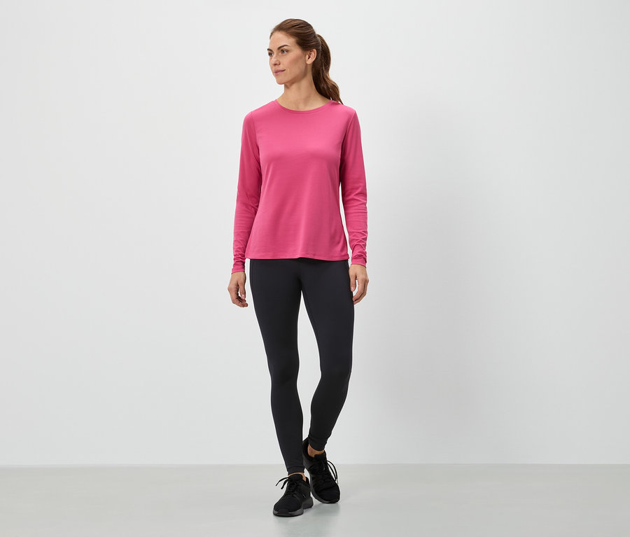 Femme debout portant un haut rose à manches longues et un legging noir.